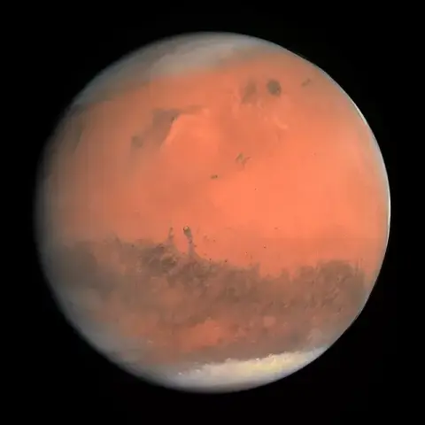 Ein Bild des Planeten Mars aufgenommen von der OSIRIS-Kamera. Der Mars erscheint als überwiegend orangefrabene Scheibe mit mehreren ausgedehnten dunkleren Flächen. Über manche Gebiete ziehen Sandstürme, die als hellere Schwaden sichtbar werden. An den Polen befinden sich ausgedehnte weisse Flächen. Die helle Planetenscheibe erscheint vor einem schwarzen Hintergrund.