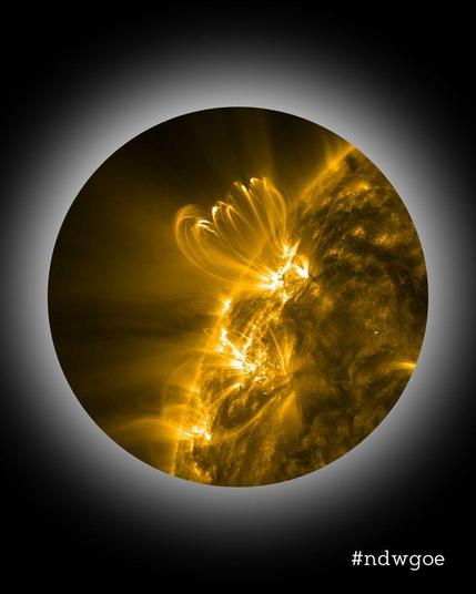 Die Sonne im extremen Ultraviolett-Licht: Ein Auschnitt der Sonnenoberfläche, eingebettet in das Nacht-des-Wissens-Design. Dabei beginnt ein schwarzer Farbgradient am äußersten Bildrand, wird hellgrau, und endet an einem kreisförmigen Bildausschnitt innen mit dunklem Hintergrund. Vor diesem Hintergrund ragt ein Ausschnitt der kreisförmigen Sonnenscheibe ins Bild. Das Bild ist in extrem-ultraviolettem Lichtt aufgenommen. Ruhige Teile der Sonnenoberfläche wirken dadurch dunkel. Ausgedehnte heiße …