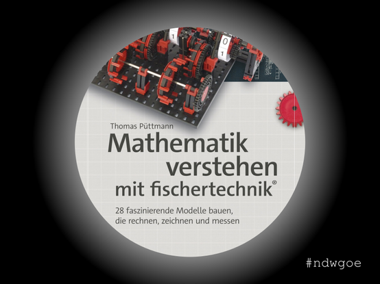 Cover des Buches "Mathematik verstehen mit fischertechnik" von Thomas Püttmann durch ein Guckloch, erschienen im dpunkt.verlag. Das Bild zeigt ein komplexes fischertechnik-Modell aus roten und schwarzen Zahnrädern, das auf einem Buch liegt. Der Titel des Buches ist groß und deutlich lesbar.