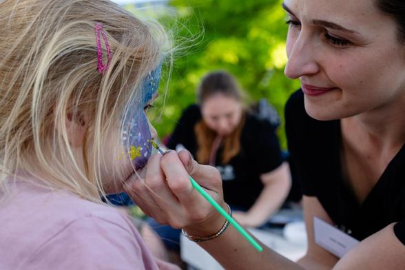 A mother and child engaged in face painting. The painting is on blue background with white and yellow stars on top.