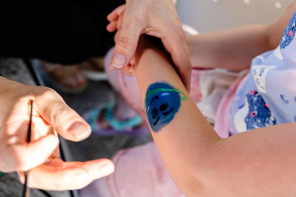 Close-up of four entangled arms, one of them with a smiling happy blue planet painted on it, and a pencil adding finishing touches.