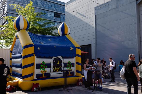 Fill view of a blue-and-yellow bouncy castle in front of a large white building in the background. People are swarming around it.
