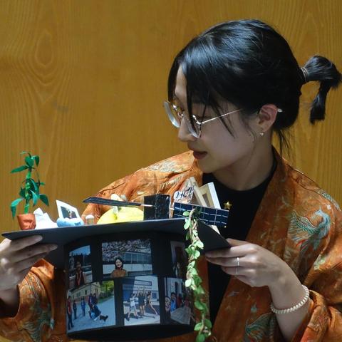 Ziwen holding her doctoral hat in front of her in both hands, looking at the various parts attached to it from above, with her mouth opening, indicating that she is currently explaining what's on the hat. 