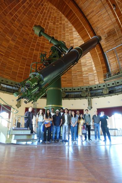 People posing for a group picture in a large cupola with a wooden roof housing a large refractor telescope.