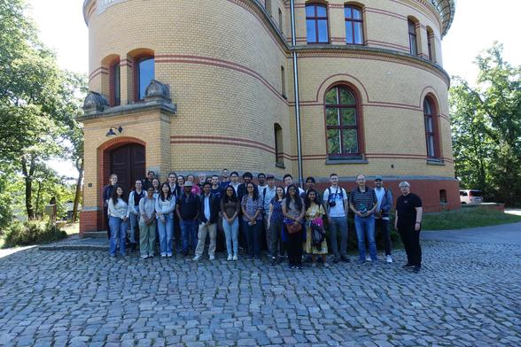 People posing for a group photo at the entrance of a historical building. It's round and extends upwards beyond the frame of the image.
