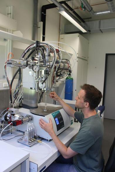 In the Knudsen cell (the small white cylinder right next to the tweezers), only a few millimeters in size, an equilibrium is established between molten rock and evaporating gas. The gas is then analyzed in the quadrupole mass spectrometer. The photograph shows Christian operating the elaborate laboratory setup.