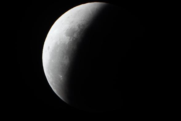 the Moon during partial lunar eclipse phase: about a third of the lunar disk appears extremely dark to the point of being almost invisible, while the non-eclipsed part is structured in brighter and darker grays (dark at the site of maria)