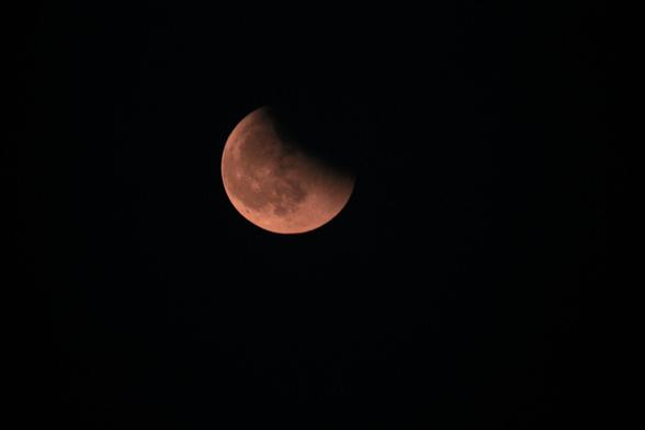 lunar disk appearing distinctly red, with a bite missing at the upper right