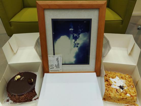 A picture of the SOHO launch, with two cakes draped left and right to the framed picture.