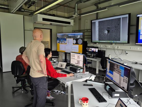 Operations center with 3 scientists working at desks and several large monitors showing the GREGOR telescope, an active region and a full-disc view of the Sun. 