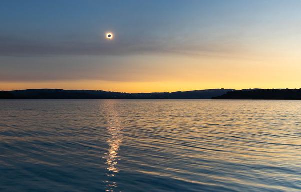 total solar eclipse over body of water with hills in the background
