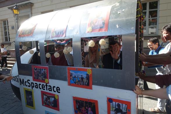 Side view of a doctoral cart showing that it's named "SpaceyMcSpaceface". People inside the cart are smiling and waving.